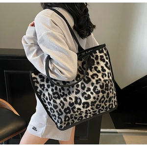 Detail view of a large leopard print tote bag with black canvas straps on a model