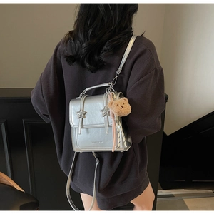 Detail of silver metallic leather backpack with star buckles and a plush bear charm