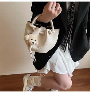Detail of beige bucket bag with litchi texture and cute plush puppy keychain charm