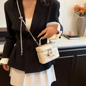 Detailed view of white quilted crossbody bag with heart pendant and metal chain strap