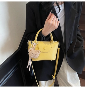 Detail of yellow lychee textured bucket bag with brown teddy bear charm and strap