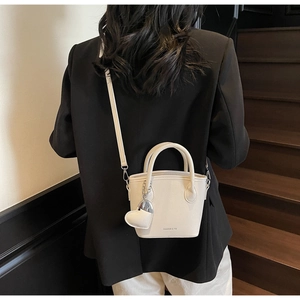Close-up of lychee grain cream bucket bag featuring heart pendant and fashion logo