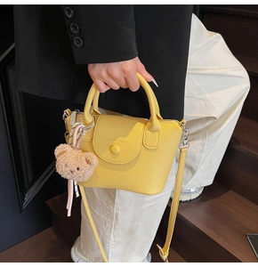 Detail of yellow lychee leather bag with plush bear charm and striped ribbon accent