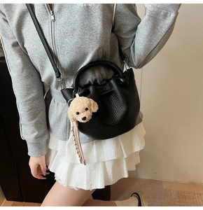 Detail of black pebbled leather bucket bag with cute dog plush charm and adjustable strap