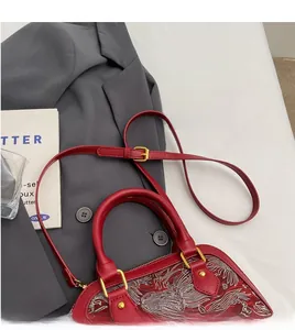 Detailed shot of red shell bag with white floral embroidery and adjustable gold buckle strap