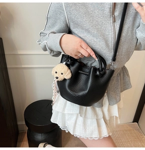 Detail of black pebbled leather bucket bag with cute plush puppy charm accessory