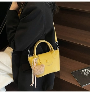 Détail du sac à main jaune à motif litchi avec charmant ours en peluche et pompon tissé