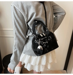 Détail du sac à main en cuir verni noir avec quincaillerie argentée et breloque en cœur