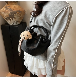 Detail of black litchi leather bucket bag featuring a beige teddy dog plush charm
