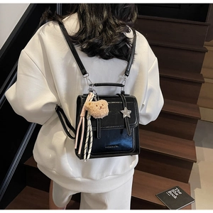 Glossy black patent leather backpack with star detail and plush bear charm on white hoodie