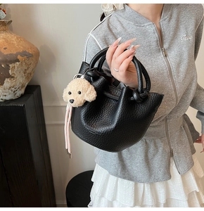 Detail of black lychee grain leather bucket bag with knotted handle and dog charm