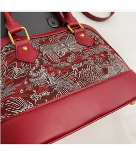 Close-up of bird embroidery and floral texture on wine red shell bag with gold hardware
