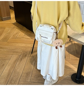 Sac bandoulière blanc avec oreilles de chat et porte-clé ours sur pull jaune