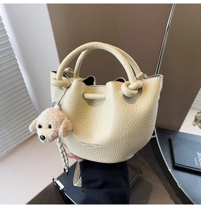 Close-up of cream lychee leather bucket bag featuring drawstring and plush dog charm