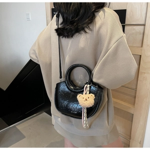 Detail of black glossy semi-circular crossbody bag with a cute beige plush bear charm