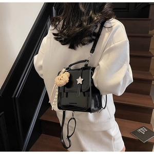 Detail of black glossy backpack with silver star decor and plush bear charm on model