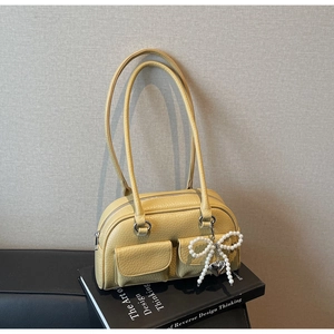 Close-up of yellow pebble leather bag with pearl bow charm and front flap pockets