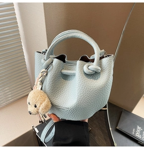 Detail of light blue bucket bag with pebble leather texture and knot handle