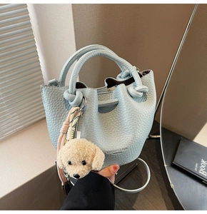 Detail of light blue bucket bag with thick knot handle and plush puppy pendant