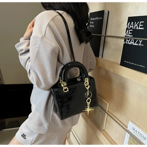 Detail of glossy black bag with embossed patterns and gold metal handles and charms