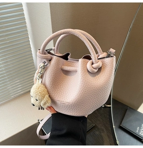 Detail of pink lychee grain bucket bag featuring a knotted handle and plush dog charm