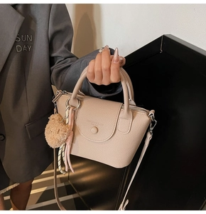 Detail of beige litchi grain handbag with plush bear charm and silk scarf handle decor