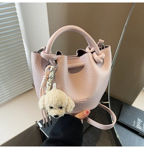 Macro detail of pink lychee leather bucket bag with dog plush charm and ring handle