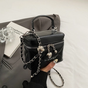 Detail of black quilted vanity bag with metal chain strap and luxury heart charm
