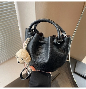 Close-up of black lychee grain leather bucket bag with cute teddy dog plush keychain