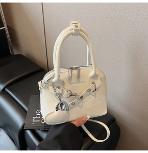 Gros plan d'un sac shell en cuir verni blanc avec pendentif cœur argenté et chaîne