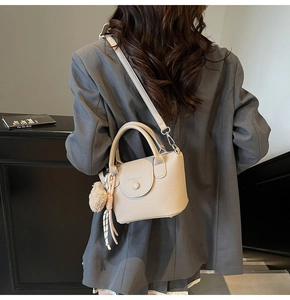 Rear view of a beige lychee leather bucket bag with a plush charm on a grey blazer