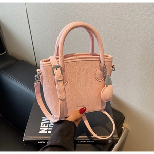 Detailed macro view of pink litchi grain leather bucket bag with heart charm and brand logo