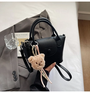 Close-up of black lychee-grain leather bucket bag with cute plush bear charm accessory