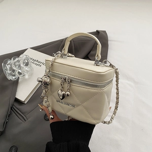 Detail of cream quilted handbag with heart charm, gold chain and metal hardware