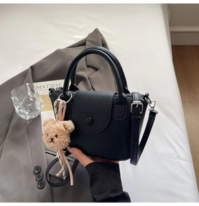 Detail of black lychee grain leather bucket bag with cute brown teddy bear charm