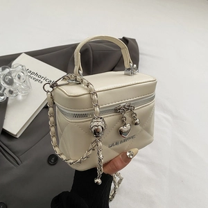 Close-up of quilted cream handbag with gold heart pendant and metal brand logo detail