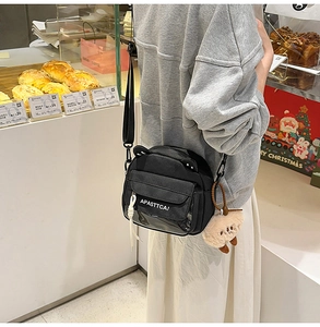 Détail du sac bandoulière en toile noire avec poche transparente et breloque ours en peluche