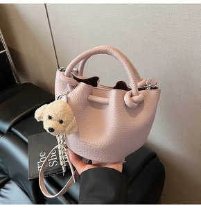 Detail of light pink lychee texture bucket bag with white puppy plush keychain charm