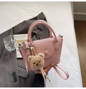 Close-up of pink lychee leather handbag with snap flap and brown plush bear charm