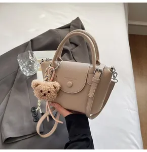 Detail of beige lychee texture bucket bag with plush bear charm and adjustable strap