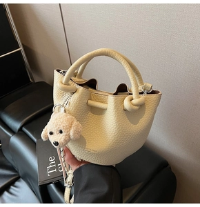 Detail of cream lychee leather bucket bag with knot handle and teddy charm