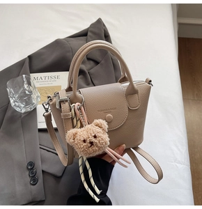 Detailed view of beige pebble leather mini bucket bag with a cute brown plush bear charm
