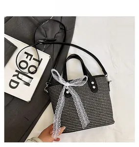 Detail of woven bucket bag with white lace bow decoration and black leather handle
