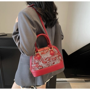 Detail of red shell bag with white floral and crane embroidery on leather and fabric