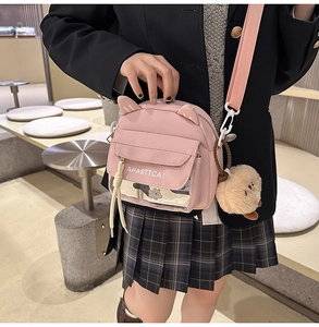 Détail d'un sac bandoulière en toile rose avec oreilles de chat et porte-clés en peluche