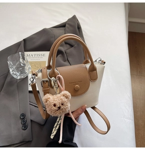 Detail of the litchi pattern leather bag featuring a fashion logo and plush bear charm