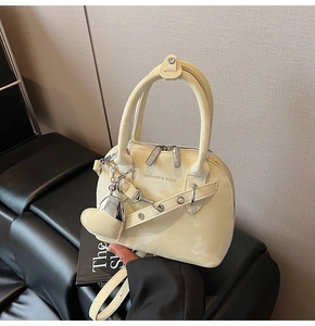 Détail du sac beige avec double fermeture éclair, chaîne en métal et charm en forme de cœur