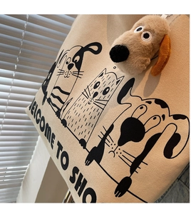 Detail of canvas tote bag featuring black cartoon illustrations and a plush dog charm