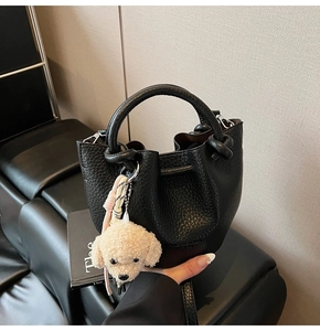 Détail du sac seau en cuir grainé noir avec un porte-clés en peluche de chien blanc mignon