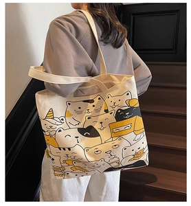Detailed view of cream canvas tote bag featuring cute cartoon cat illustrations